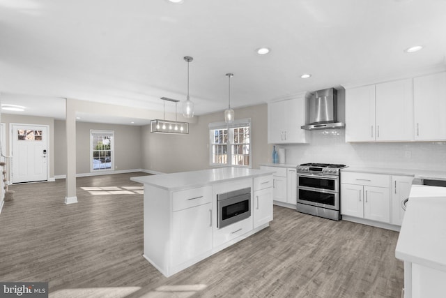 kitchen with light hardwood / wood-style flooring, a center island, wall chimney range hood, white cabinetry, and appliances with stainless steel finishes