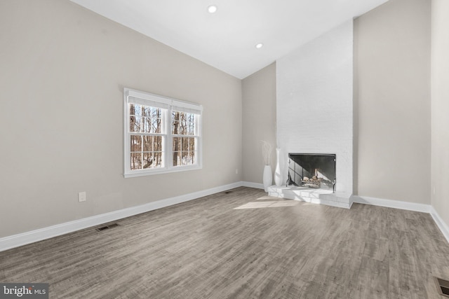 unfurnished living room featuring a large fireplace, lofted ceiling, and hardwood / wood-style flooring