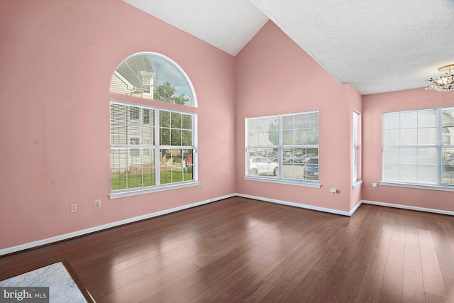 empty room with high vaulted ceiling, dark wood-type flooring, a chandelier, and a textured ceiling