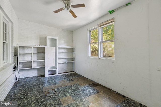 unfurnished living room with ceiling fan and brick wall