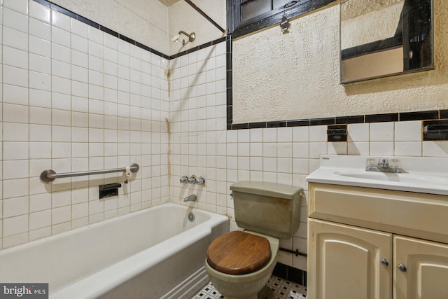 full bathroom featuring toilet, tiled shower / bath, vanity, and tile walls