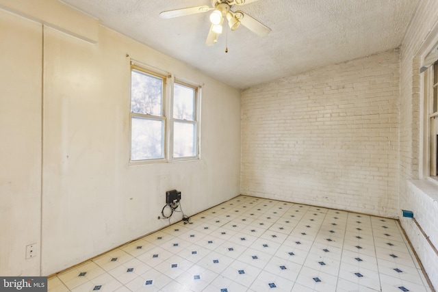 spare room featuring ceiling fan, brick wall, a textured ceiling, and vaulted ceiling