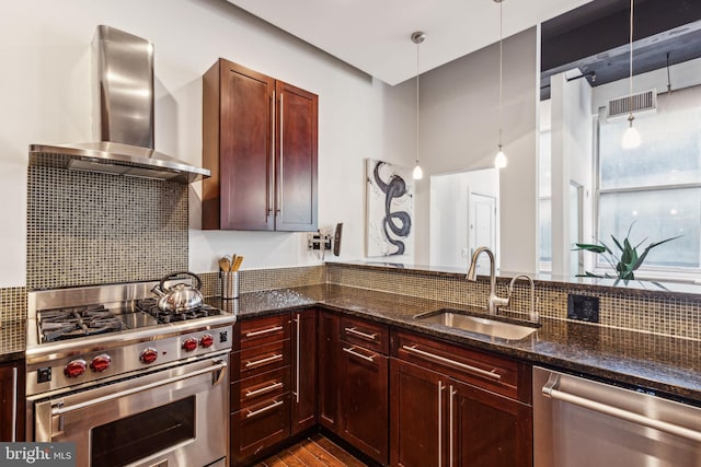 kitchen with pendant lighting, dark stone counters, sink, wall chimney exhaust hood, and stainless steel appliances