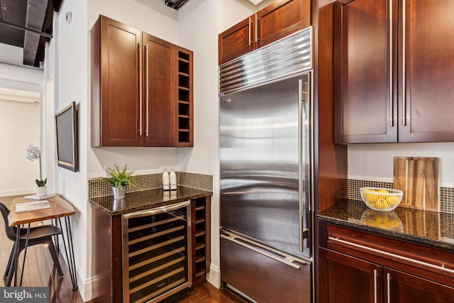 kitchen featuring dark hardwood / wood-style floors, dark stone countertops, stainless steel built in refrigerator, and beverage cooler