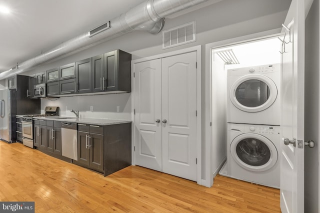 clothes washing area with sink, light hardwood / wood-style flooring, and stacked washer and clothes dryer