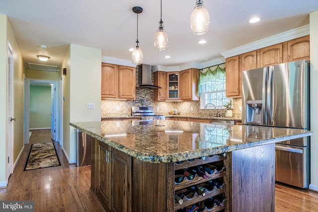 kitchen with appliances with stainless steel finishes, wall chimney exhaust hood, dark stone countertops, and light hardwood / wood-style floors