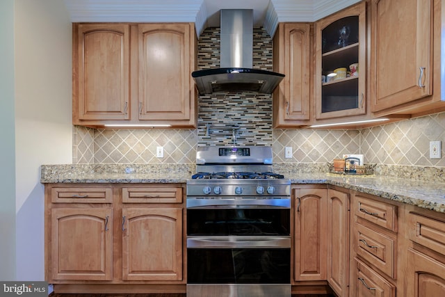 kitchen featuring light stone counters, stainless steel gas range, tasteful backsplash, and wall chimney range hood