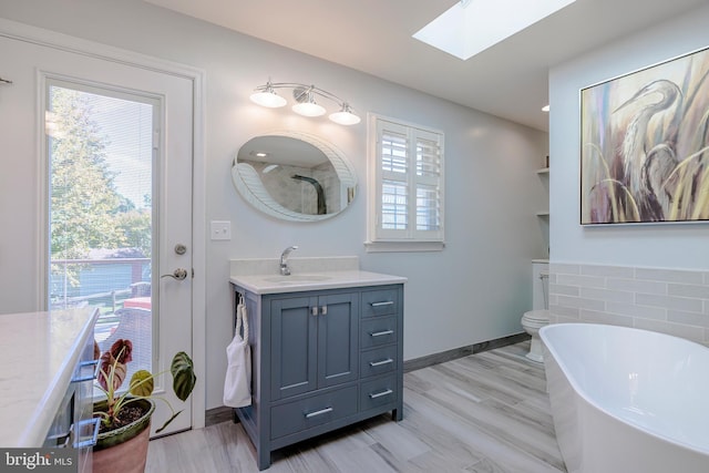 bathroom featuring vanity, wood-type flooring, a bathing tub, a skylight, and toilet