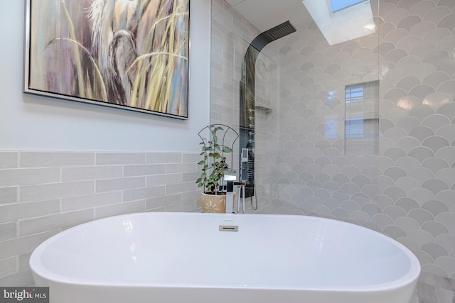 bathroom featuring a skylight, a bathing tub, and tile walls