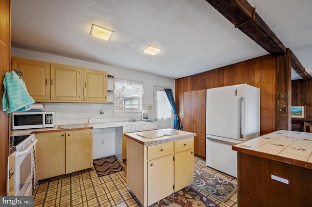 kitchen with sink, a textured ceiling, white appliances, wooden walls, and a kitchen island