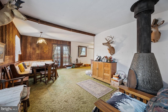 living room with wooden walls, beam ceiling, a wood stove, and carpet floors