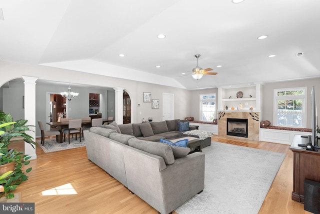 living room featuring light wood-type flooring, ceiling fan with notable chandelier, decorative columns, lofted ceiling, and a fireplace