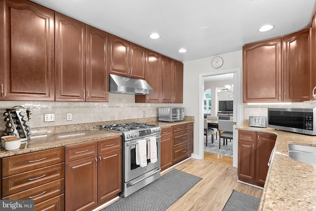 kitchen with light wood-type flooring, light stone counters, stainless steel appliances, and tasteful backsplash