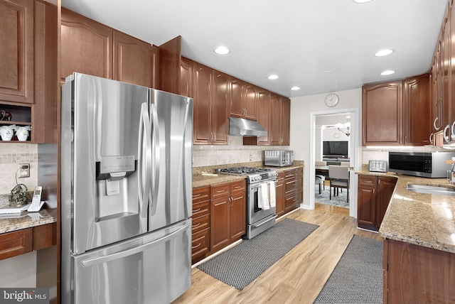 kitchen featuring light stone counters, stainless steel appliances, backsplash, and light hardwood / wood-style flooring