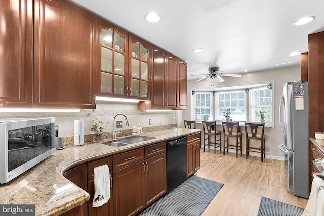 kitchen featuring light stone counters, sink, stainless steel appliances, light wood-type flooring, and decorative backsplash