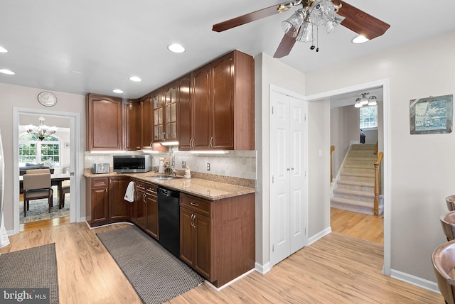 kitchen featuring light wood-type flooring, light stone countertops, decorative backsplash, ceiling fan with notable chandelier, and black dishwasher