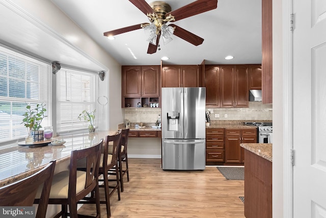 kitchen featuring light stone counters, decorative backsplash, exhaust hood, light hardwood / wood-style floors, and appliances with stainless steel finishes