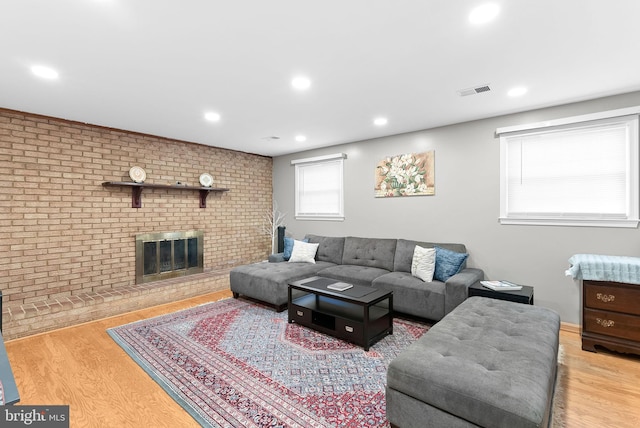 living room featuring a brick fireplace, light hardwood / wood-style flooring, and brick wall