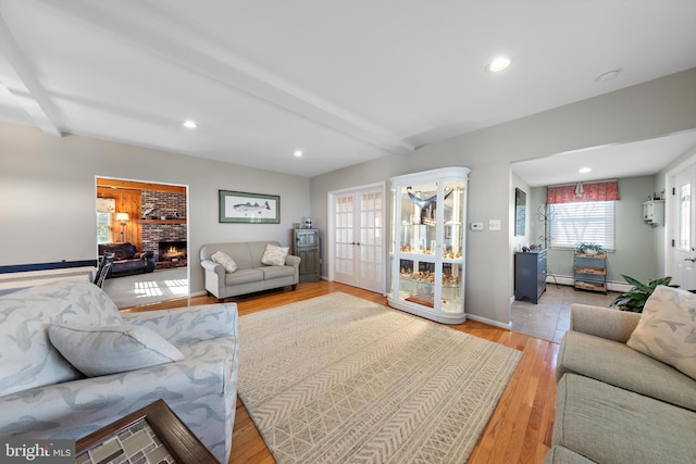 living room featuring french doors, beamed ceiling, light hardwood / wood-style flooring, and a fireplace