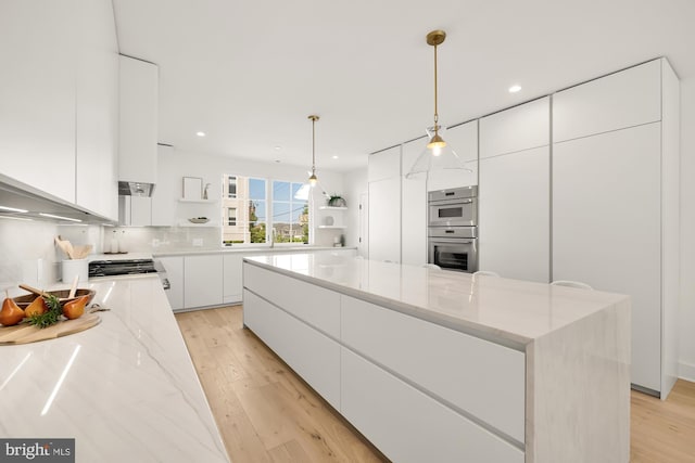 kitchen with pendant lighting, white cabinets, a large island, double oven, and light hardwood / wood-style floors