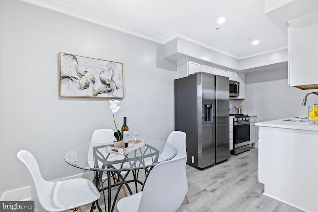 kitchen featuring white cabinets, sink, ornamental molding, stainless steel appliances, and light wood-type flooring