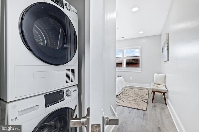 laundry area with stacked washing maching and dryer and light hardwood / wood-style flooring