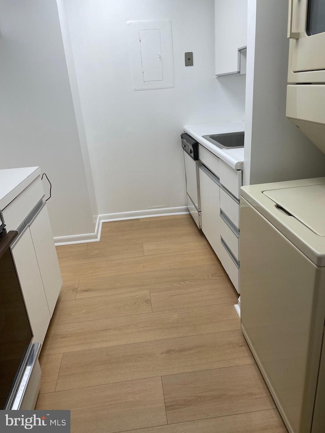 kitchen with light hardwood / wood-style flooring, stacked washer and clothes dryer, dishwasher, electric panel, and white cabinetry