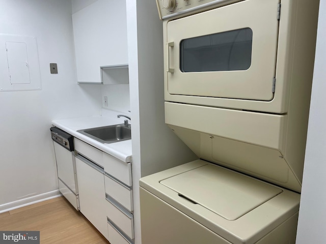 clothes washing area with light wood-type flooring, electric panel, stacked washer / drying machine, and sink