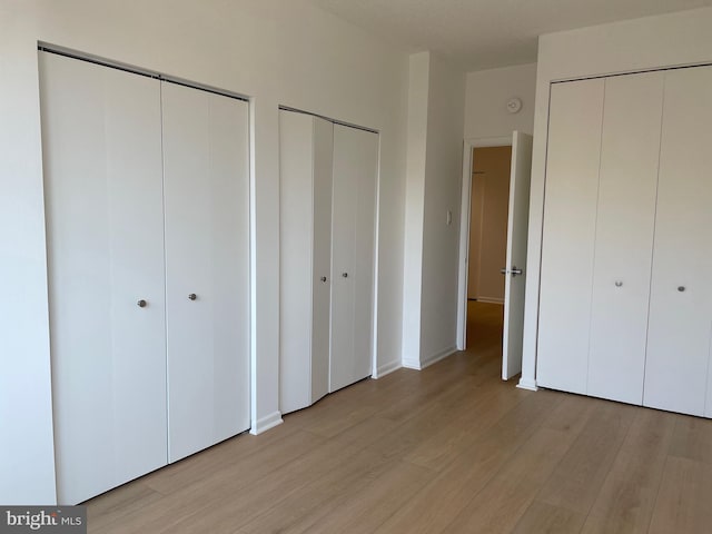 unfurnished bedroom featuring light hardwood / wood-style floors and two closets