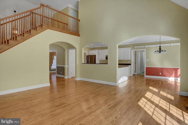 unfurnished living room featuring light hardwood / wood-style floors, a high ceiling, and a chandelier