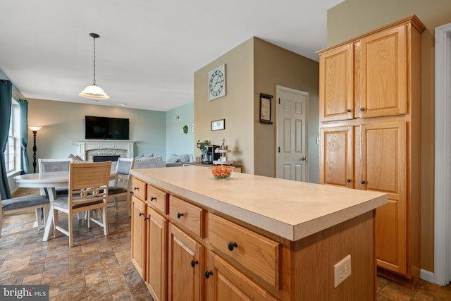 kitchen with light brown cabinetry, a stone fireplace, hanging light fixtures, and a kitchen island