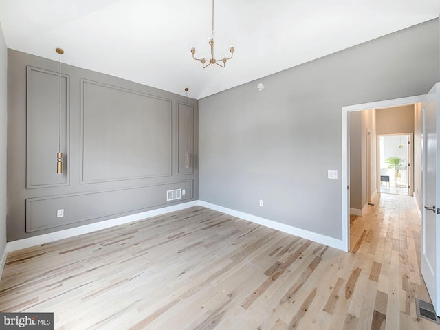 spare room featuring a notable chandelier and light hardwood / wood-style flooring