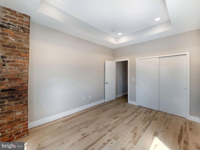 unfurnished bedroom featuring a closet, light hardwood / wood-style flooring, and a raised ceiling