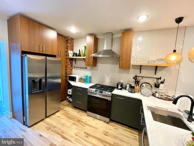 kitchen featuring wall chimney range hood, light hardwood / wood-style flooring, decorative light fixtures, sink, and appliances with stainless steel finishes