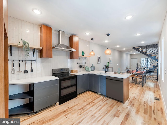 kitchen with wall chimney exhaust hood, light hardwood / wood-style floors, pendant lighting, kitchen peninsula, and black appliances