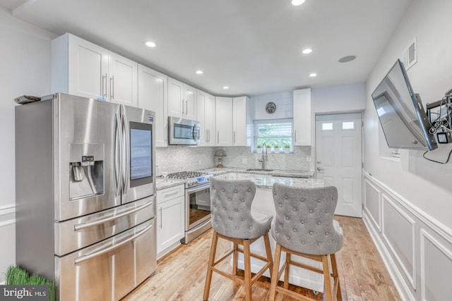 kitchen featuring white cabinetry, light stone counters, light hardwood / wood-style floors, and stainless steel appliances