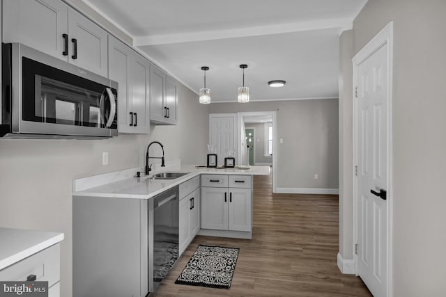 kitchen with decorative light fixtures, sink, kitchen peninsula, appliances with stainless steel finishes, and hardwood / wood-style flooring