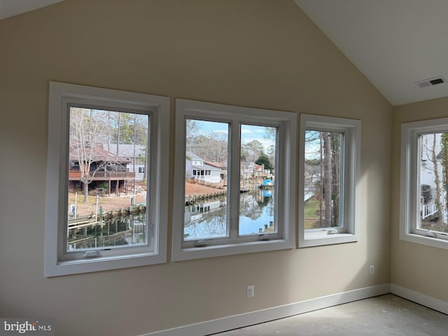 empty room with vaulted ceiling, concrete flooring, and a water view