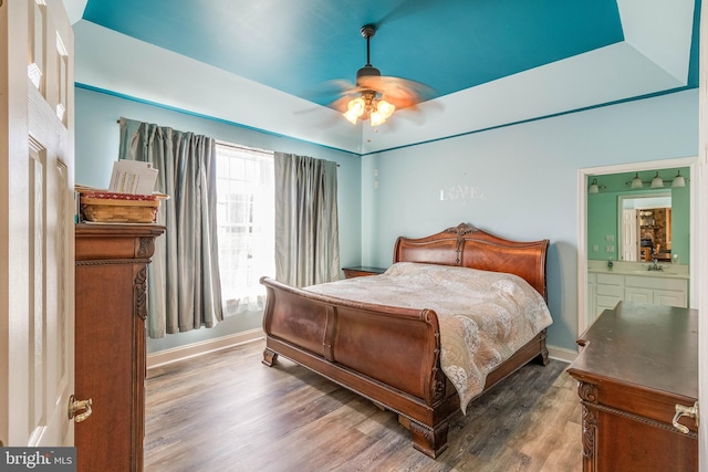 bedroom featuring ceiling fan, dark hardwood / wood-style floors, a raised ceiling, sink, and ensuite bath