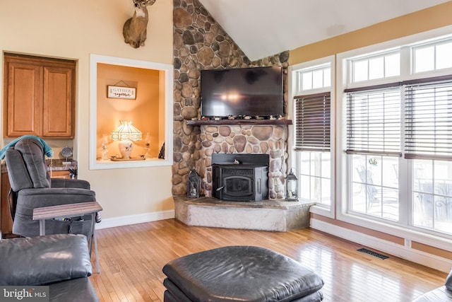 living room featuring a wood stove, high vaulted ceiling, a wealth of natural light, and light hardwood / wood-style flooring