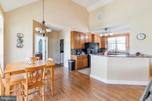 kitchen with hanging light fixtures, kitchen peninsula, light hardwood / wood-style flooring, backsplash, and high vaulted ceiling