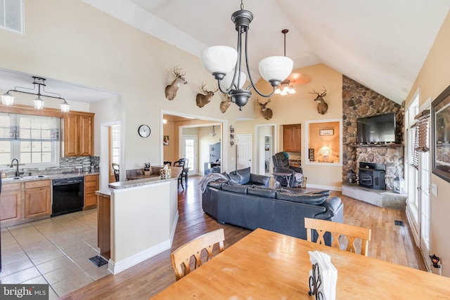 dining space featuring sink, light hardwood / wood-style flooring, a wood stove, and high vaulted ceiling