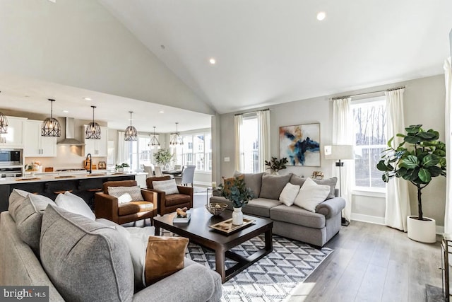 living room featuring high vaulted ceiling, an inviting chandelier, light wood-type flooring, and sink