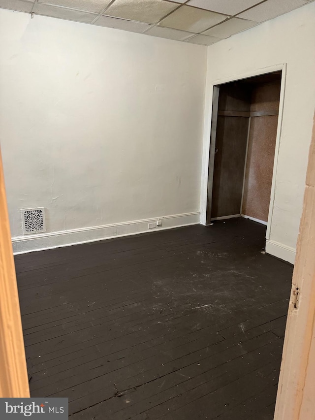 unfurnished bedroom with a drop ceiling, a closet, and dark hardwood / wood-style flooring