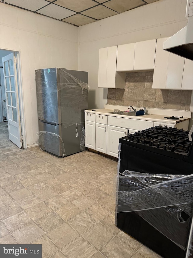 kitchen featuring black range, white cabinetry, stainless steel refrigerator, range hood, and decorative backsplash