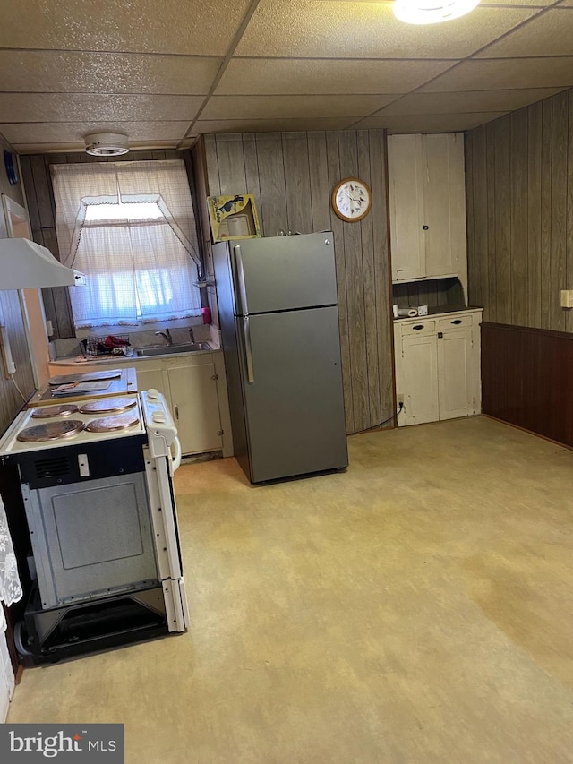 kitchen featuring stainless steel fridge, a paneled ceiling, stove, wooden walls, and white cabinets