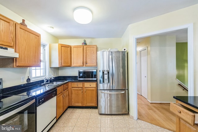 kitchen with stainless steel appliances, under cabinet range hood, a sink, and dark countertops