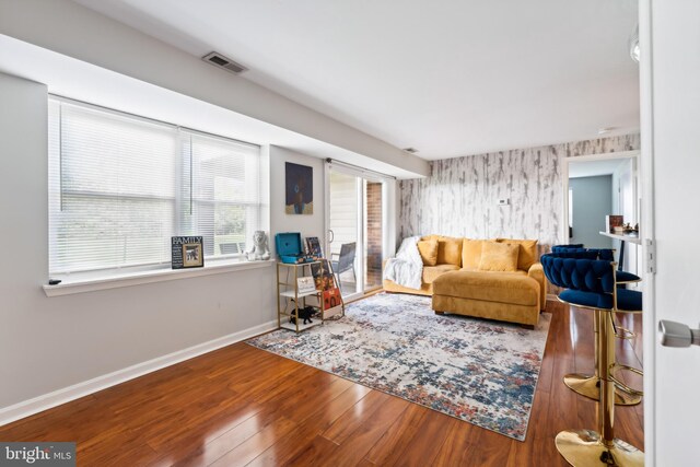 living room with visible vents, baseboards, wood finished floors, and wallpapered walls