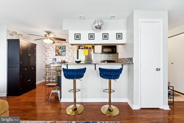 kitchen with wood finished floors, a breakfast bar, refrigerator, ceiling fan, and black microwave