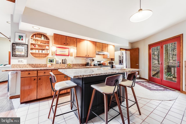 kitchen featuring stainless steel appliances, light stone countertops, a center island, pendant lighting, and light tile patterned floors